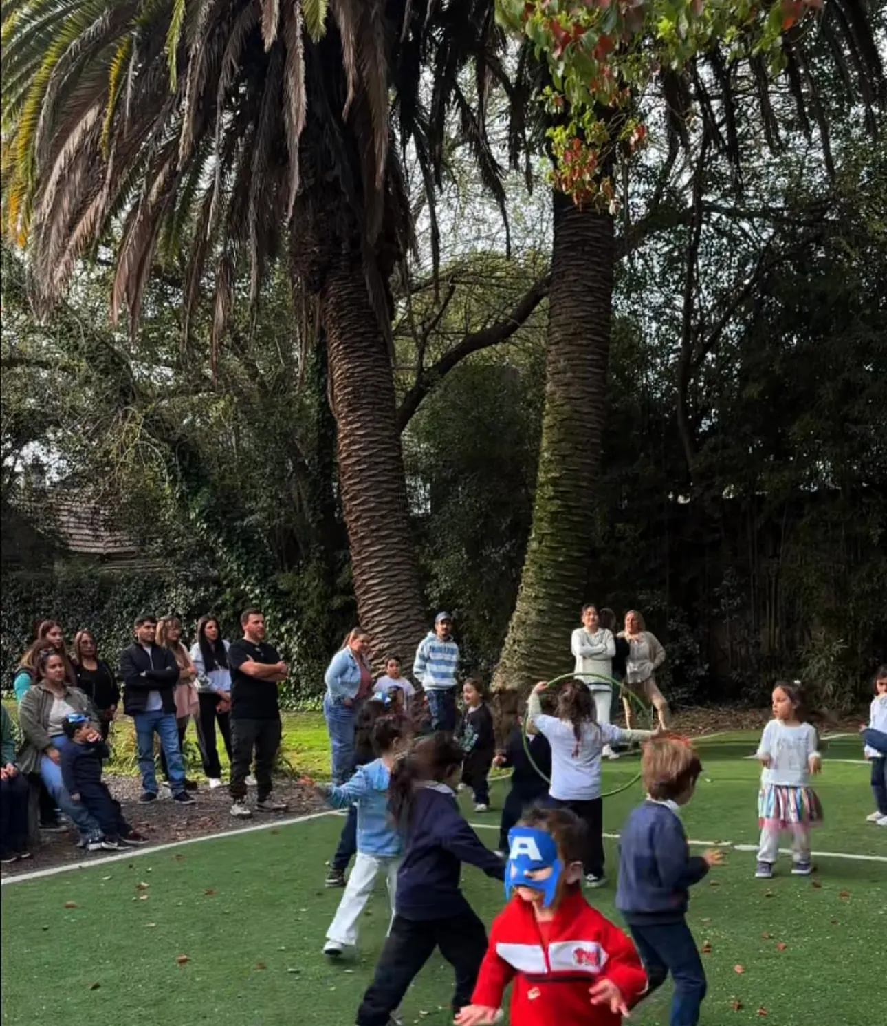Grupo de chicos corriendo y jugando en la cancha con el parque de fondo