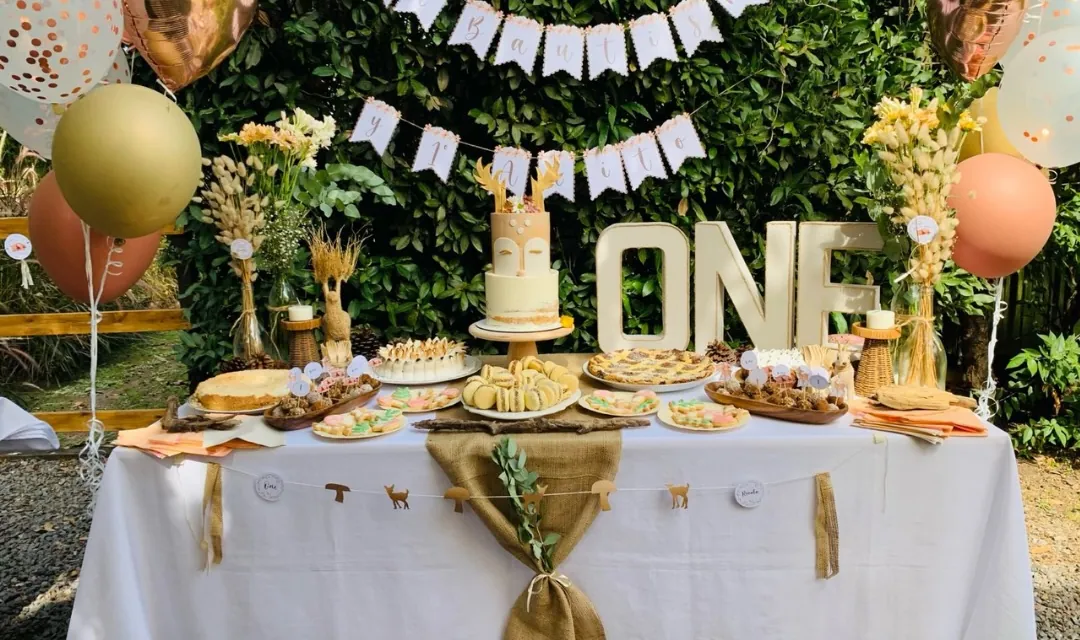 Mesa dulce de un bautismo y primer año al aire libre, con torta, globos y guirnaldas